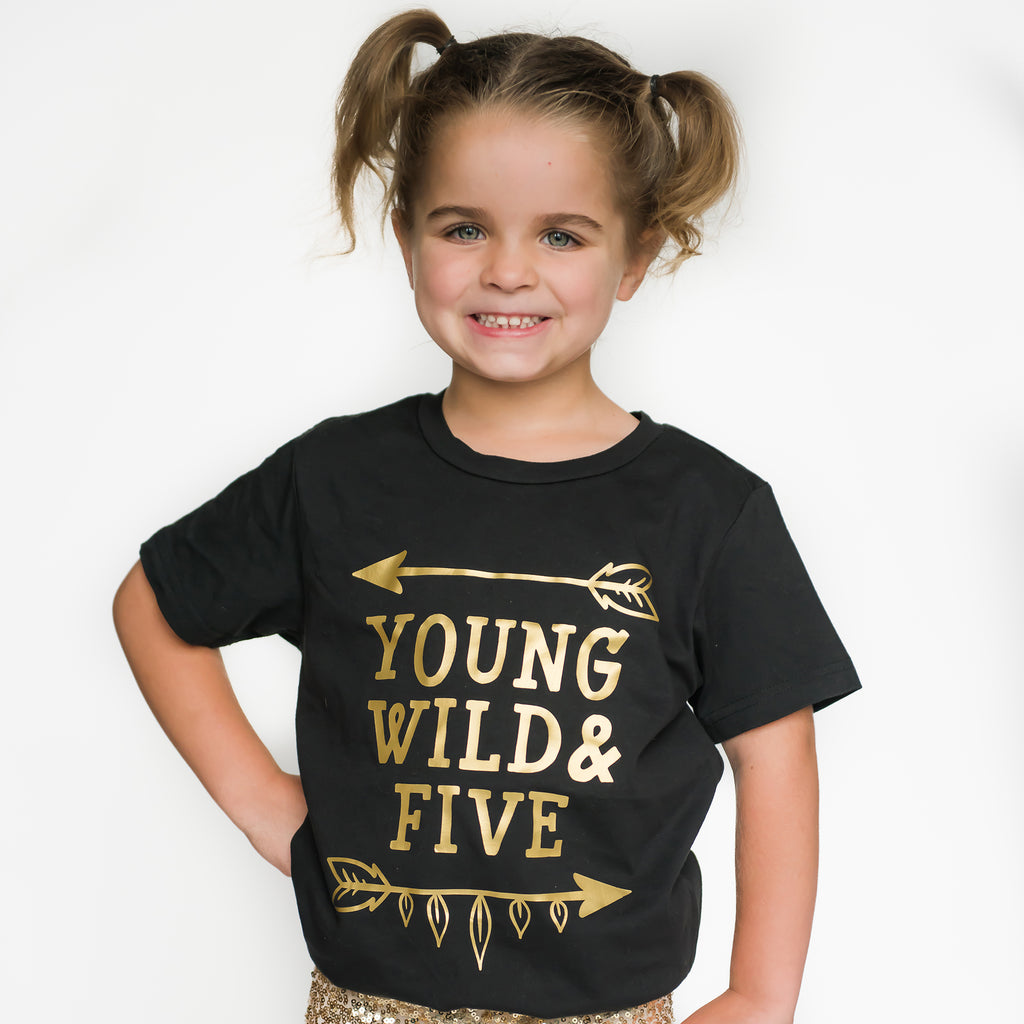 Little girl wearing black short sleeve shirt that says Young Wild and Five with arrow above and below in shiny gold