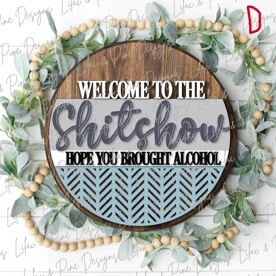 Round wooden door hanger with angled pattern cuts in bottom half that says Welcome to the Shitshow Hope you brought alcohol in brown, grey, darker grey, blue , white and black