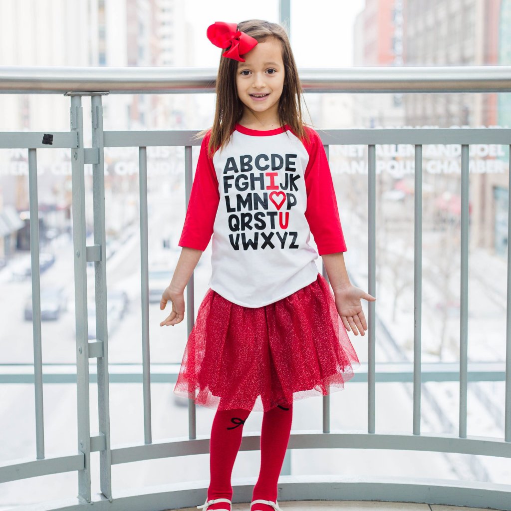 Little girl wearing red sleeve raglan with alphabet in black and I heart U in red 