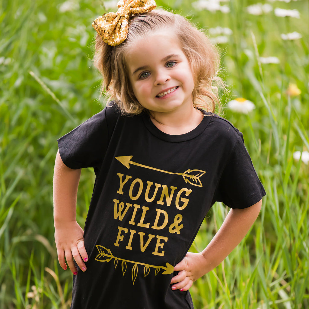 Girl wearing black young wild and five t-shirt with gold writing in a field of flowers